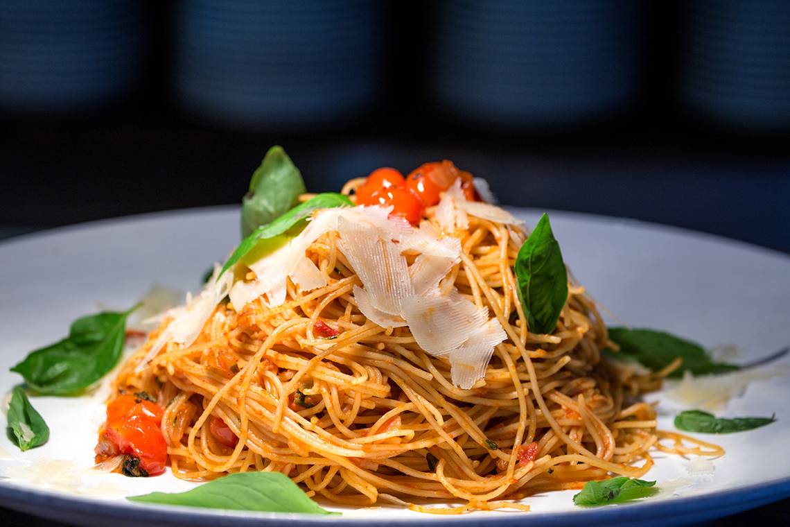 Spaghettigericht mit Tomaten und Basilikum auf einem weißen Teller.