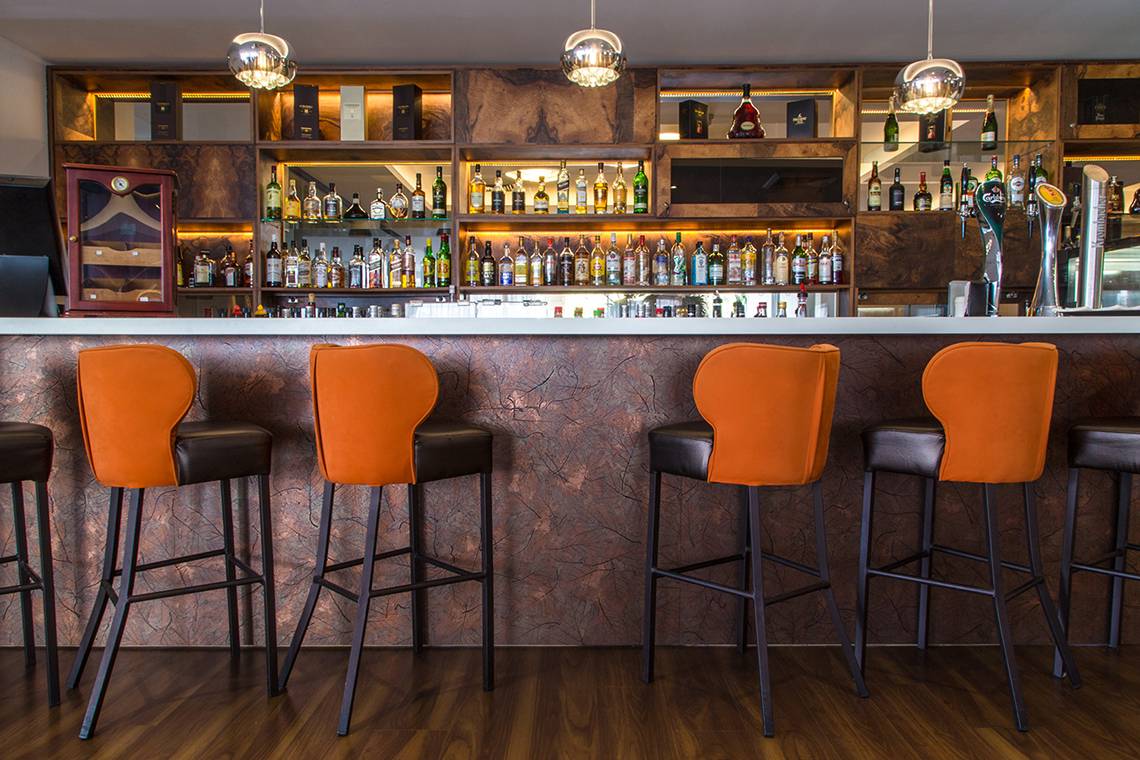 Innenansicht der Bar im Lordos Beach Hotel mit orangefarbenen Stühlen und einer großen Auswahl an Getränken.