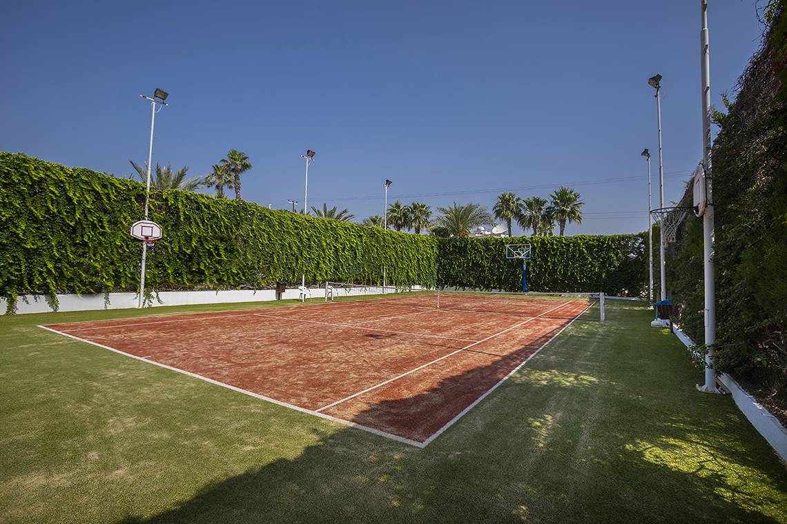 Tennisplatz im Freien des Lordos Beach Hotels, umgeben von grünen Hecken und Palmen.