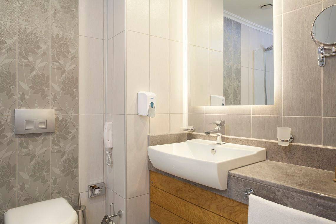 Badezimmer im Side Orange Palace Hotel mit weißem Waschbecken, Spiegel und Fliesen.