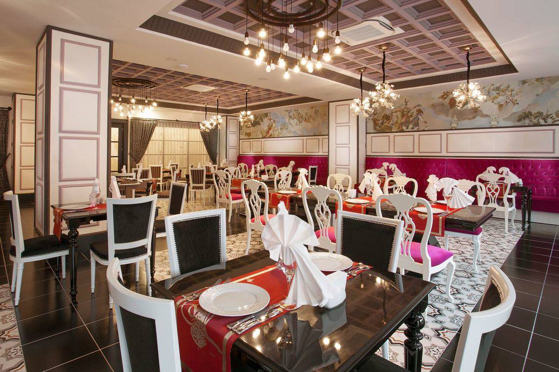 Innenansicht des Restaurants im Side Orange Palace Hotel mit Tisch und Stühlen, kunstvollen Deckenlampen und Wandgemälden.