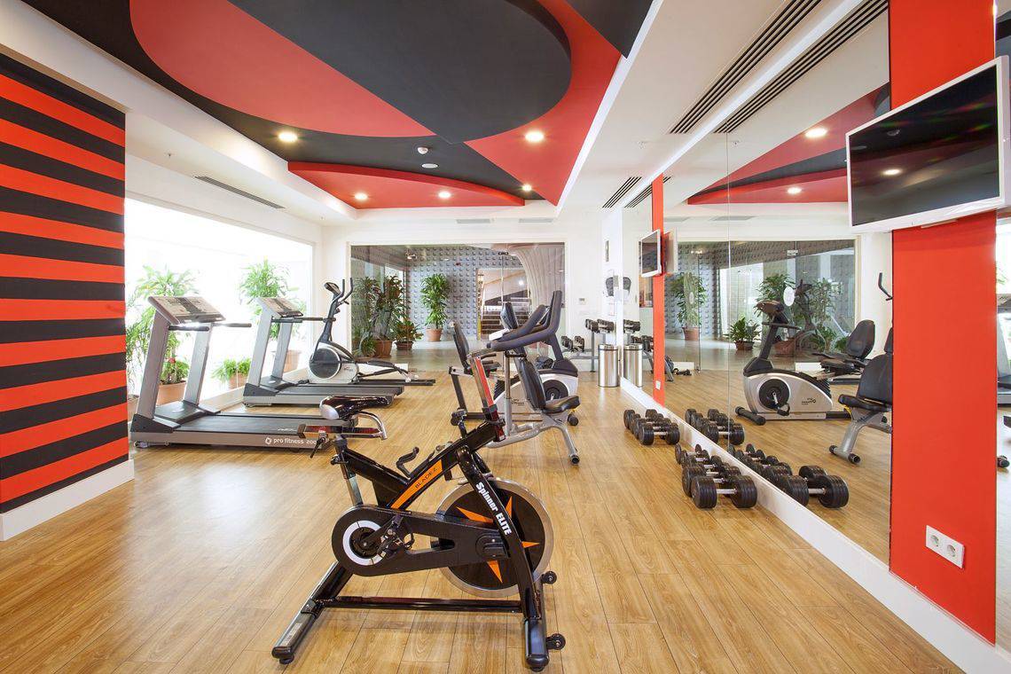 Fitnessraum im Side Orange Palace Hotel mit verschiedenen Trainingsgeräten und roten Wänden.