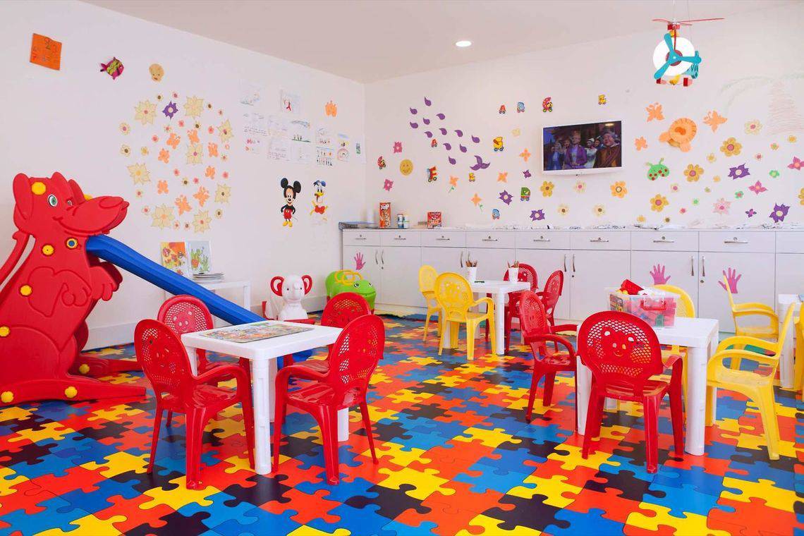 Kinderspielzimmer im Side Orange Palace mit bunten Puzzle-Boden, Tischen, Stühlen und Spielzeug.