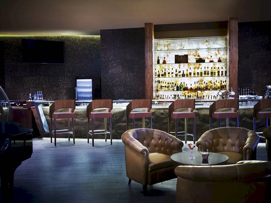 Barbereich im Sofitel Dubai The Palm mit Holzstühlen und einer großen Bar.