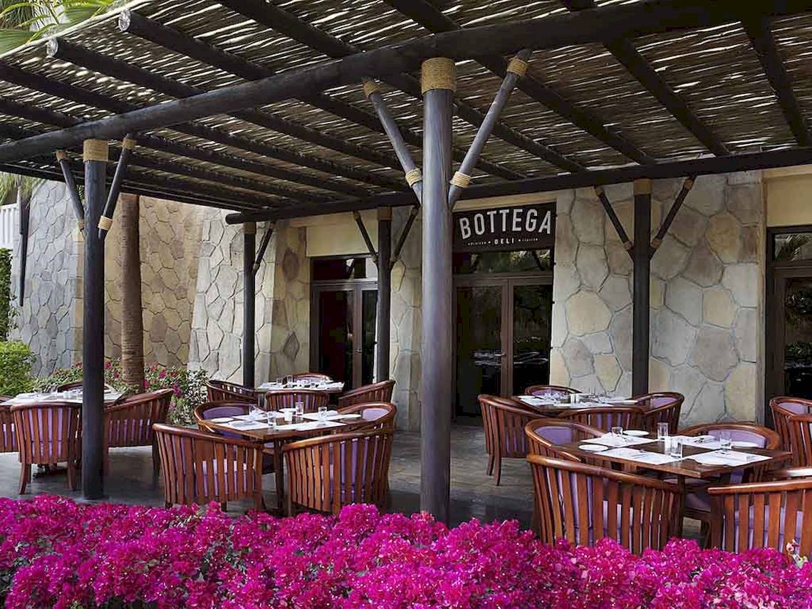 Außenbereich des Restaurants Bottega Deli im Sofitel Dubai The Palm mit holzigen Tischen und Stühlen unter einem Dach.