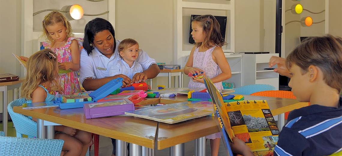 Eine Mitarbeiterin des Trou aux Biches Beachcomber Golf Resort & Spa hilft Kindern beim Basteln an einem Tisch.
