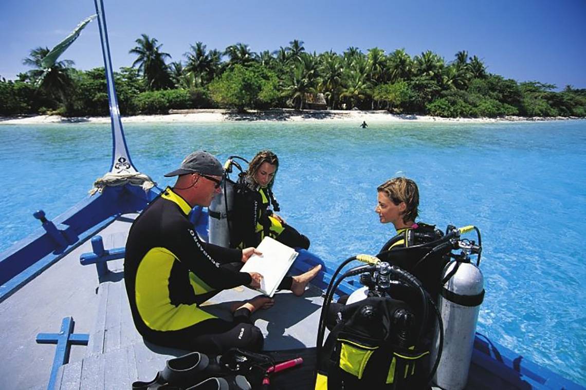 Drei Taucher sitzen auf einem Boot vor einer Insel und lesen einen Plan.