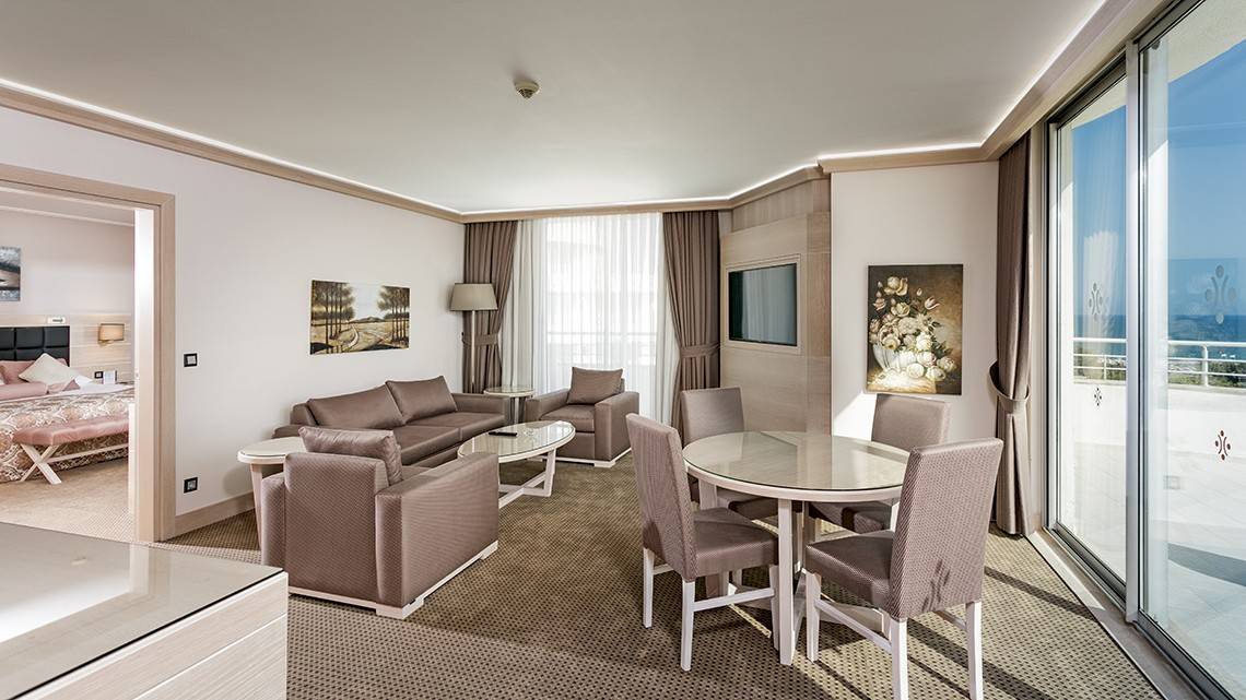 Innenansicht eines Suite-Wohnzimmers im Miracle Resort mit Couch, Esstisch und Meerblick.