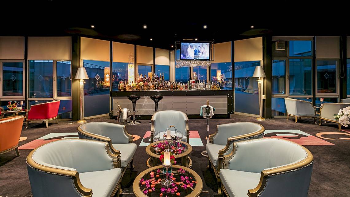 Lounge-Bereich im Miracle Resort mit Bar, Fernseher, Sesseln und Tisch mit Blumendekor.