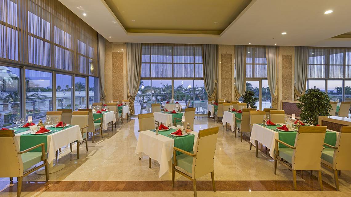 Restaurant im Miracle Resort mit großen Fenstern und grünen Tischdecken.