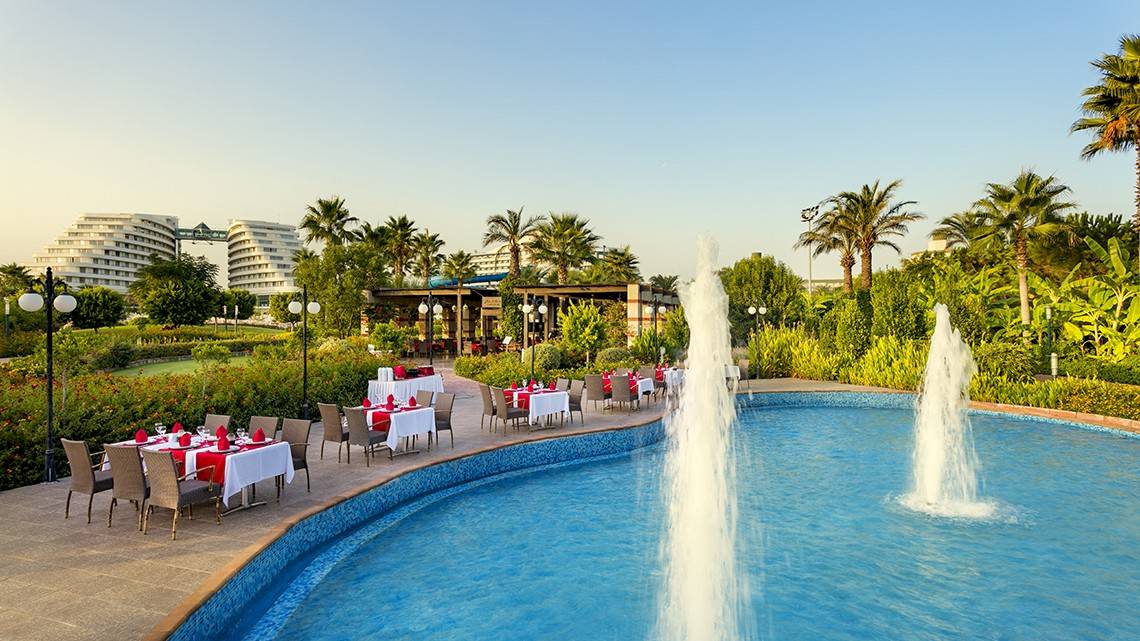 Außenbereich des Miracle Resorts mit Swimmingpool, Tischen und Palmen.