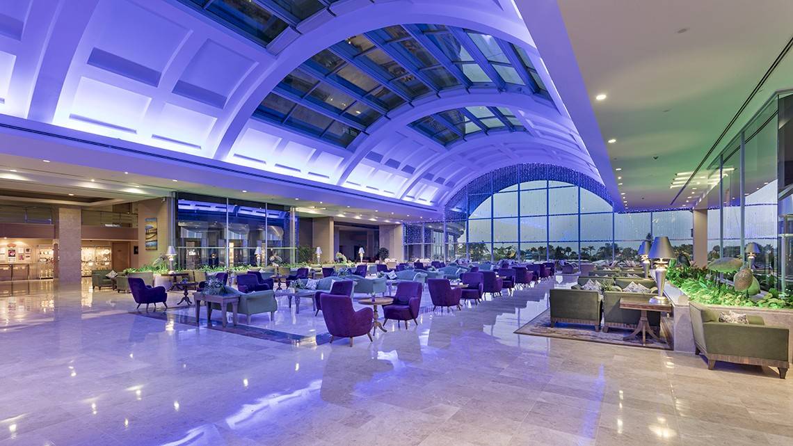 Innenansicht der Lobby des Miracle Resort Hotels mit violetter Beleuchtung und vielen Möbeln.