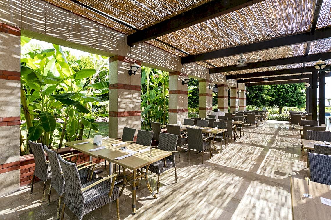 Außenterrasse des Miracle Resorts mit Tischen und Stühlen, überdacht und von Pflanzen umgeben.