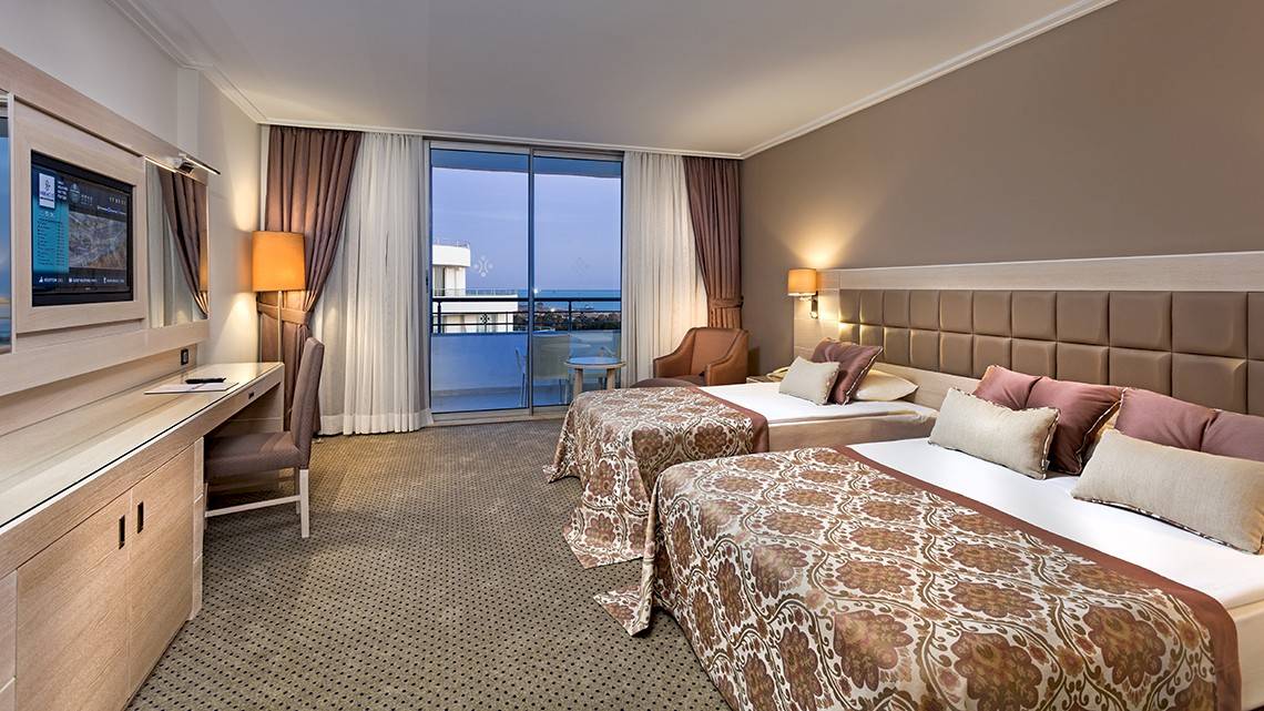 Doppelzimmer im Miracle Resort mit Balkon und Meerblick, zwei Betten, Schreibtisch, Fernseher und großem Fenster.