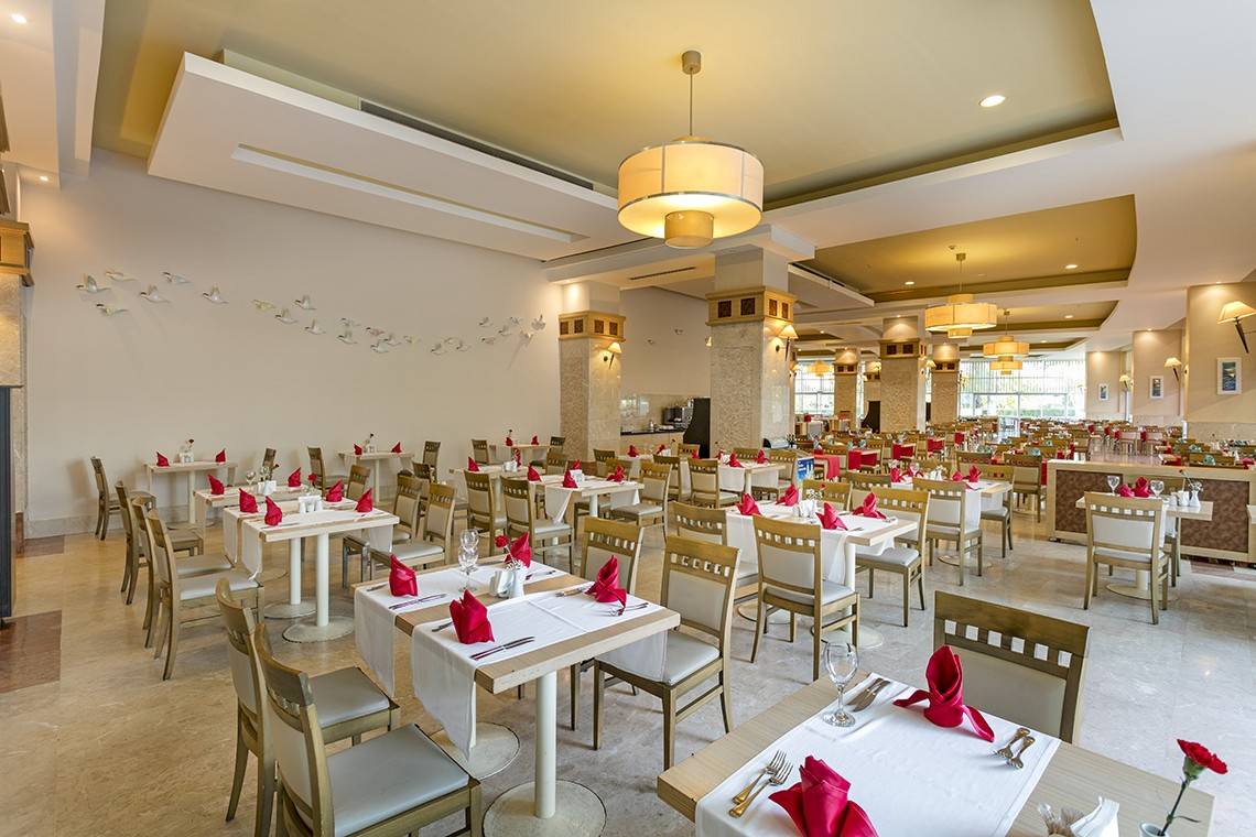 Restaurant im Miracle Resort mit vielen gedeckten Tischen und Stühlen, heller Einrichtung und dekorativen Vögeln an der Wand.