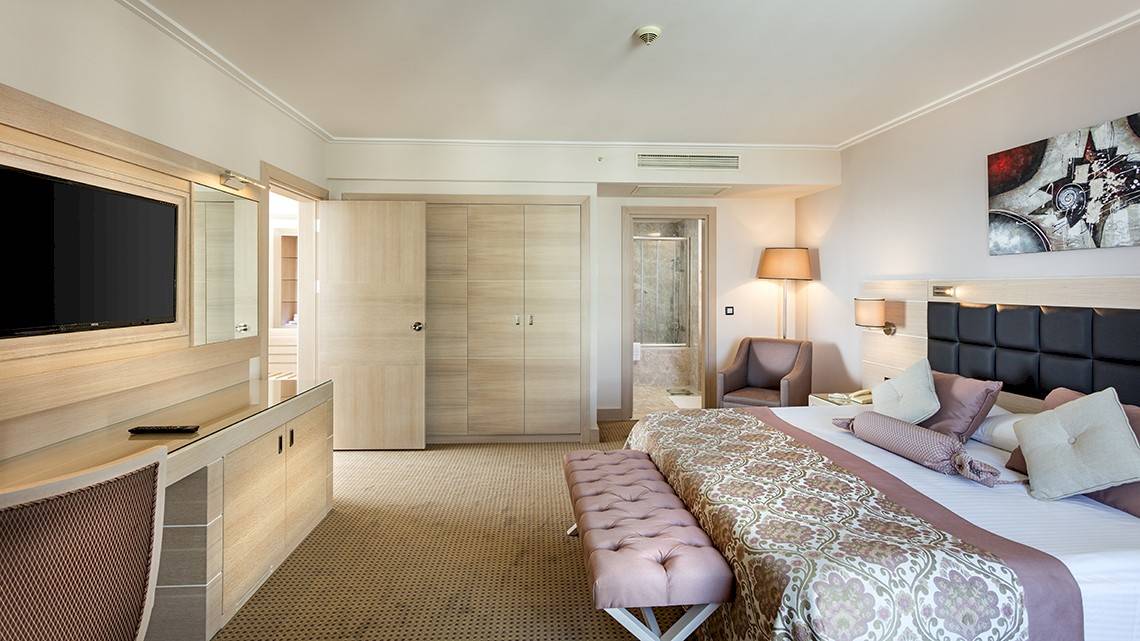 Innenansicht eines luxuriösen Hotelzimmers im Miracle Resort mit Bett, Fernseher, Schreibtisch und Möbeln.
