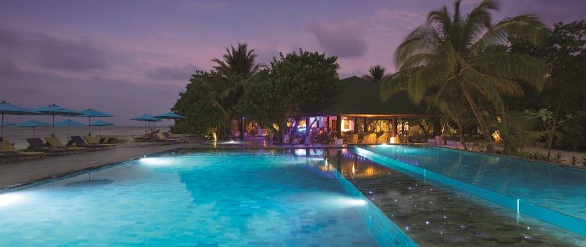 Pool im OBLU NATURE Helengeli Hotel mit Loungeliegen und beleuchteten Bäumen in der Nacht