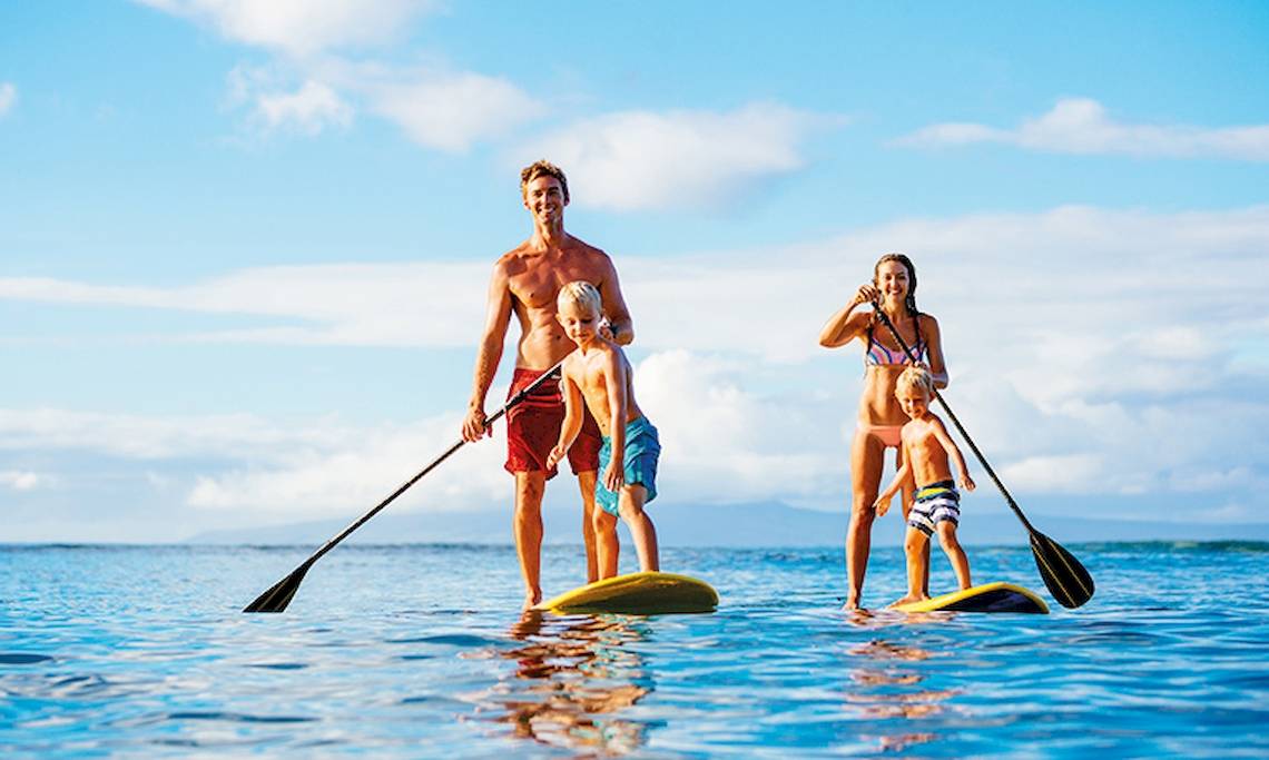Eine Familie auf Stand-Up-Paddle-Brettern im Wasser, mit klarem Himmel im Hintergrund.