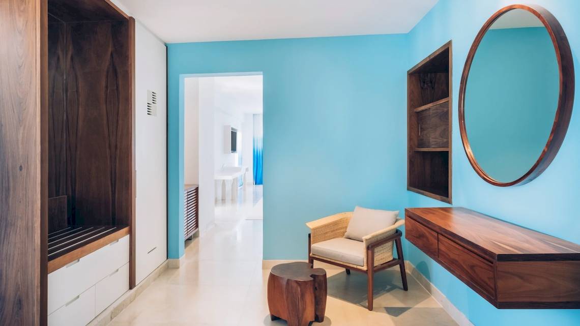 Innenansicht der Suite im Coral Level at Iberostar Selection Cancun mit blauen Wänden, einem Holzstuhl und einem Spiegel.