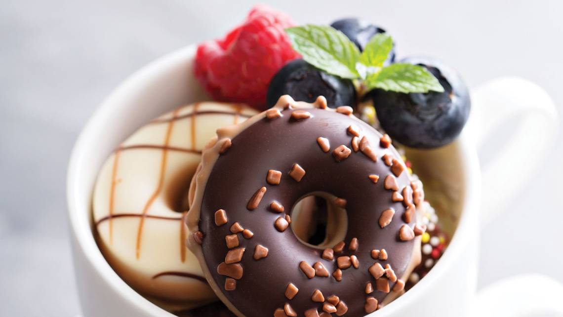 Ein weißer Becher mit Schokoladen-Donuts, gefüllt mit verschiedenen Beeren und Minzblättern.