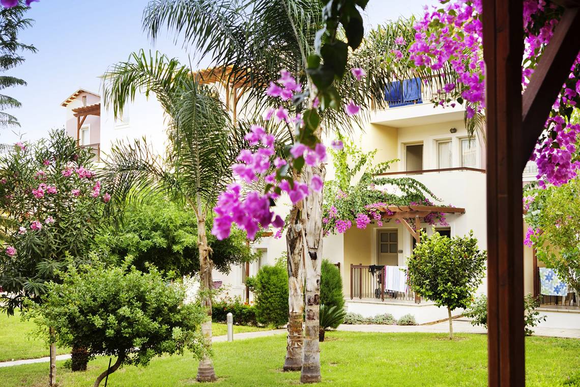 Außenansicht des Louis Althea Beach Hotels mit grünem Rasen und blühenden Pflanzen.