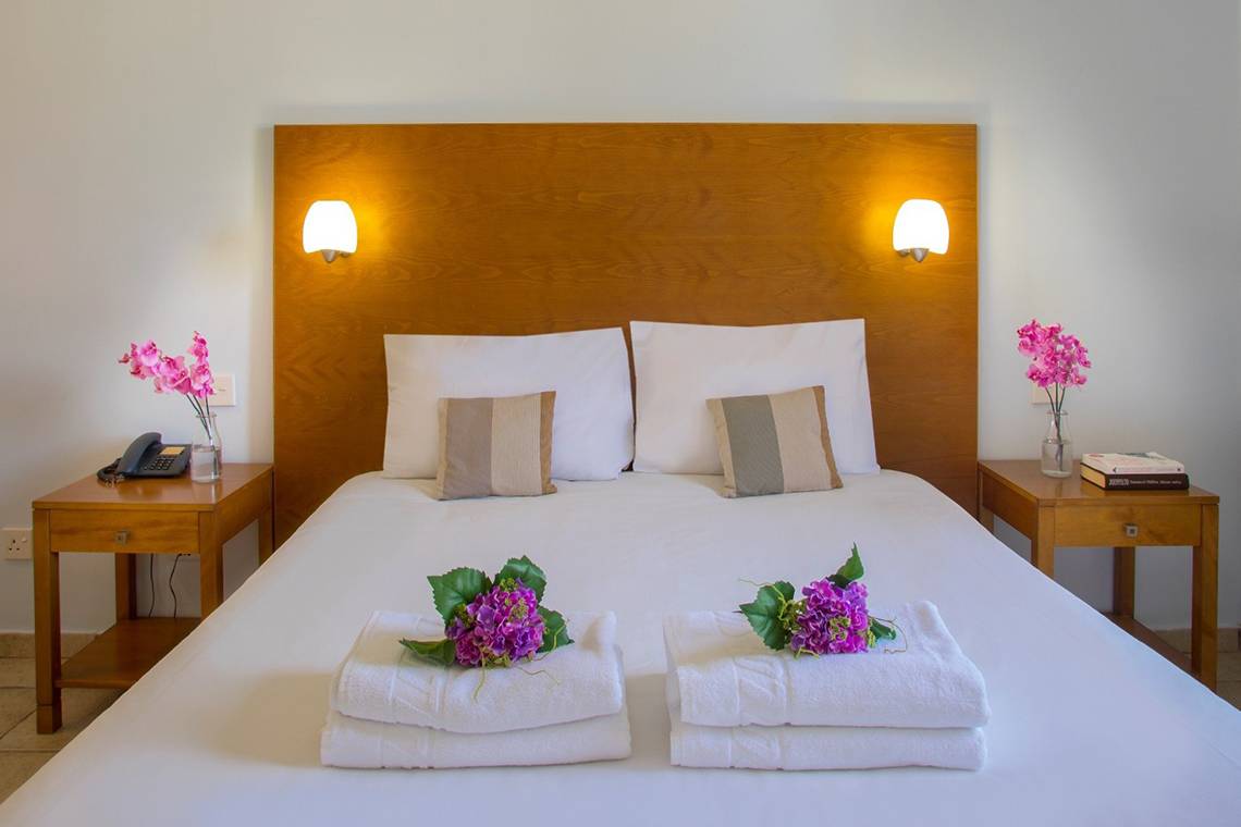 Bett im Louis Althea Beach Hotel Zimmer mit weißen Laken, Kissen und Blumen.