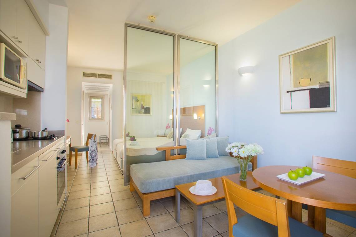 Innenansicht einer Suite im Louis Althea Beach Hotel mit Küche, Schlafbereich und Esstisch.