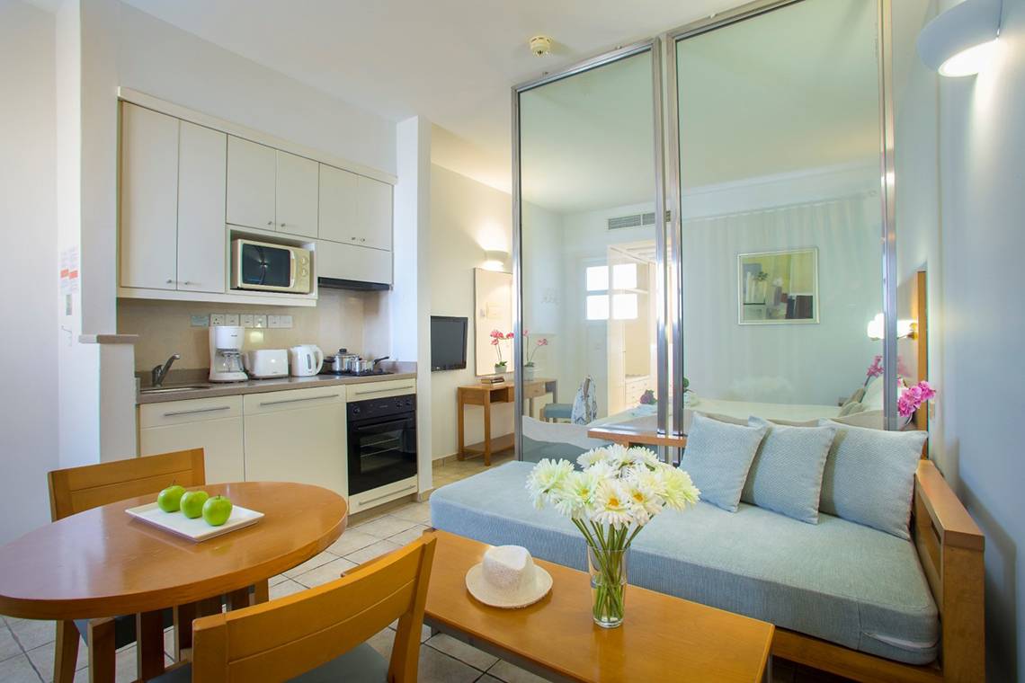 Inneneinrichtung des Louis Althea Beach Hotels mit Küchenbereich, Esstisch, Sofa und Blumenvase.
