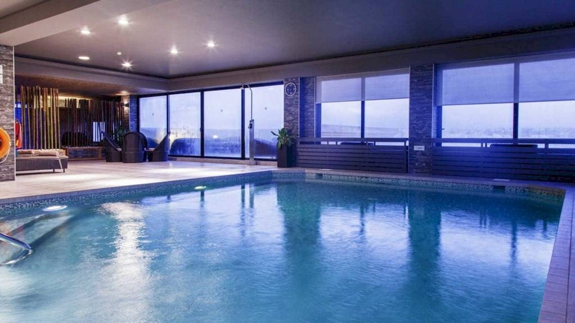 Innenpool des AX The Palace Hotels mit großen Fenstern und Loungebereich.