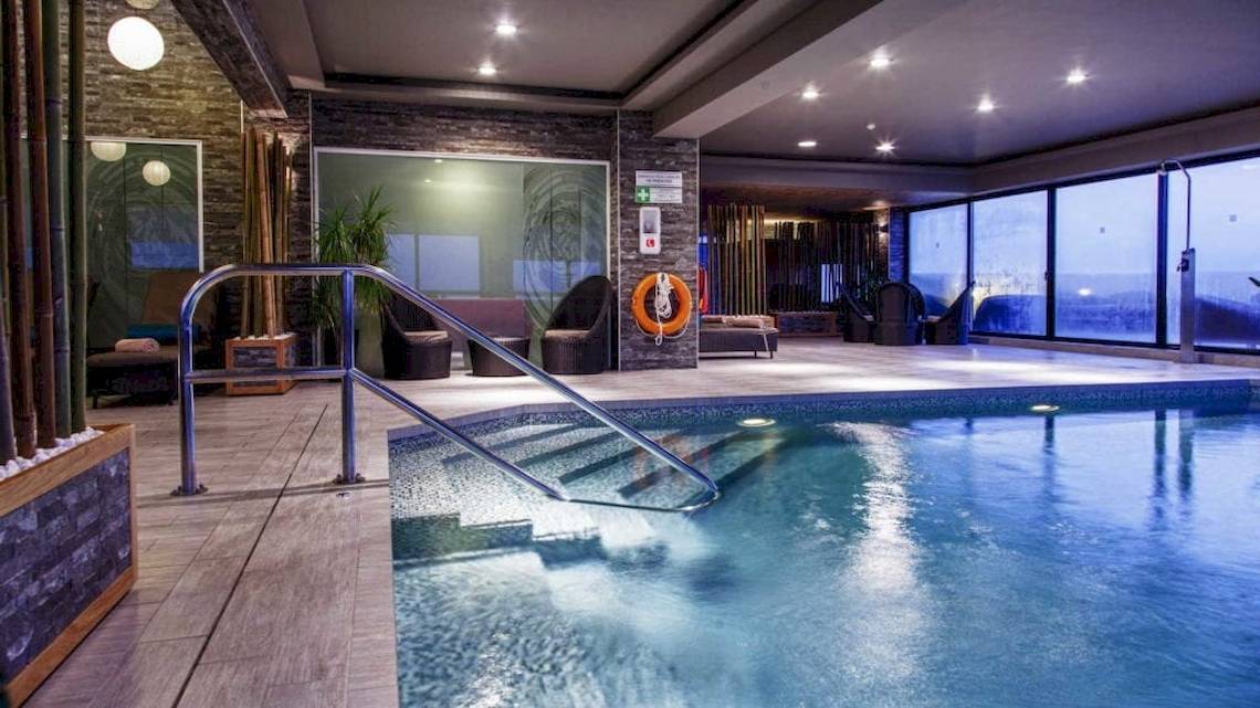Innenpool des AX The Palace Hotels mit modernen Möbeln und Glaswänden.