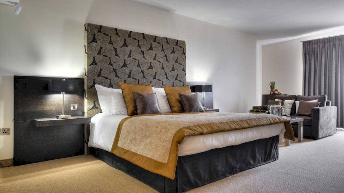 Schlafzimmer im AX The Palace Hotel mit großem Bett, dekorativen Kissen und Nachttischen.
