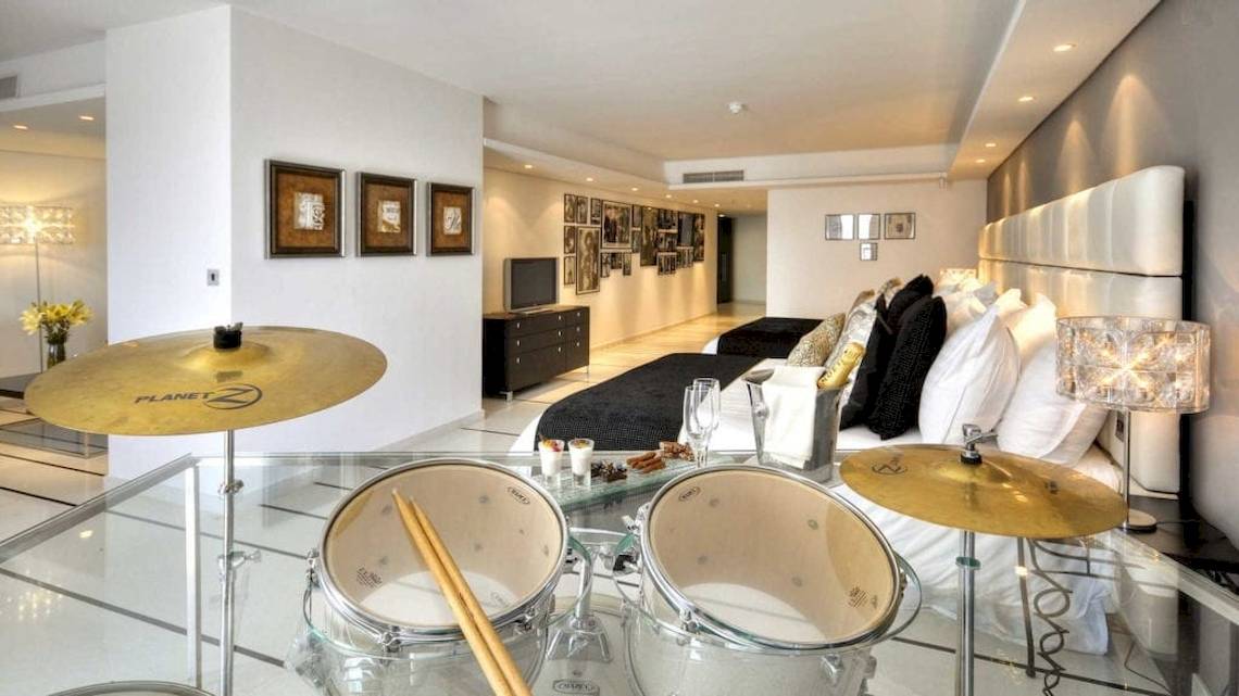 Schlafzimmer im AX The Palace Hotel mit einem Bett, weißen Kissen und einer Drum-Set auf einem Glastisch.