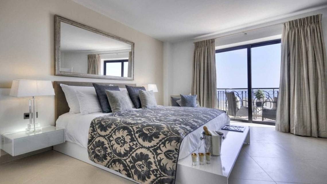 Schlafzimmer im AX The Palace Hotel mit einem großen Bett, vielen Kissen, und einem Balkon mit Meerblick.