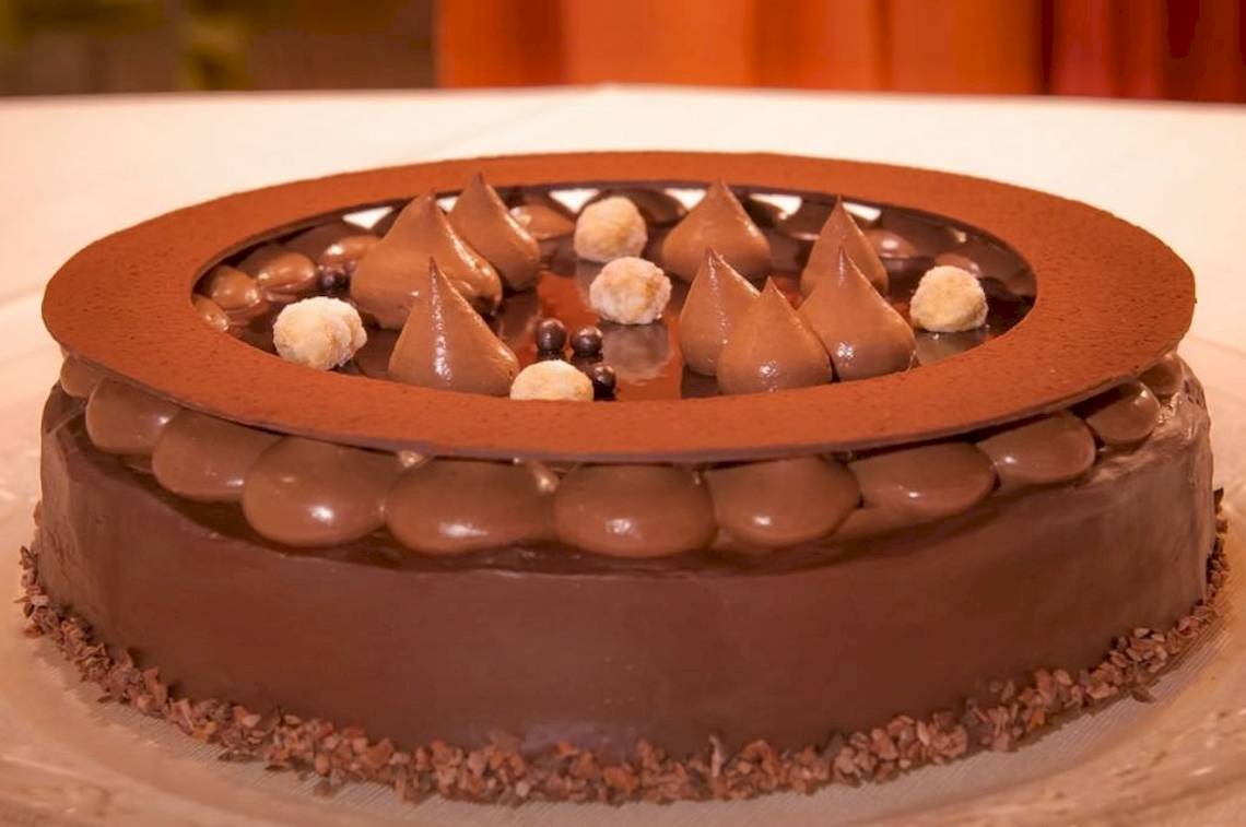 Ein Schokoladenkuchen mit Schokoladenherzen und Makronen obenauf, auf einem Glasteller serviert.