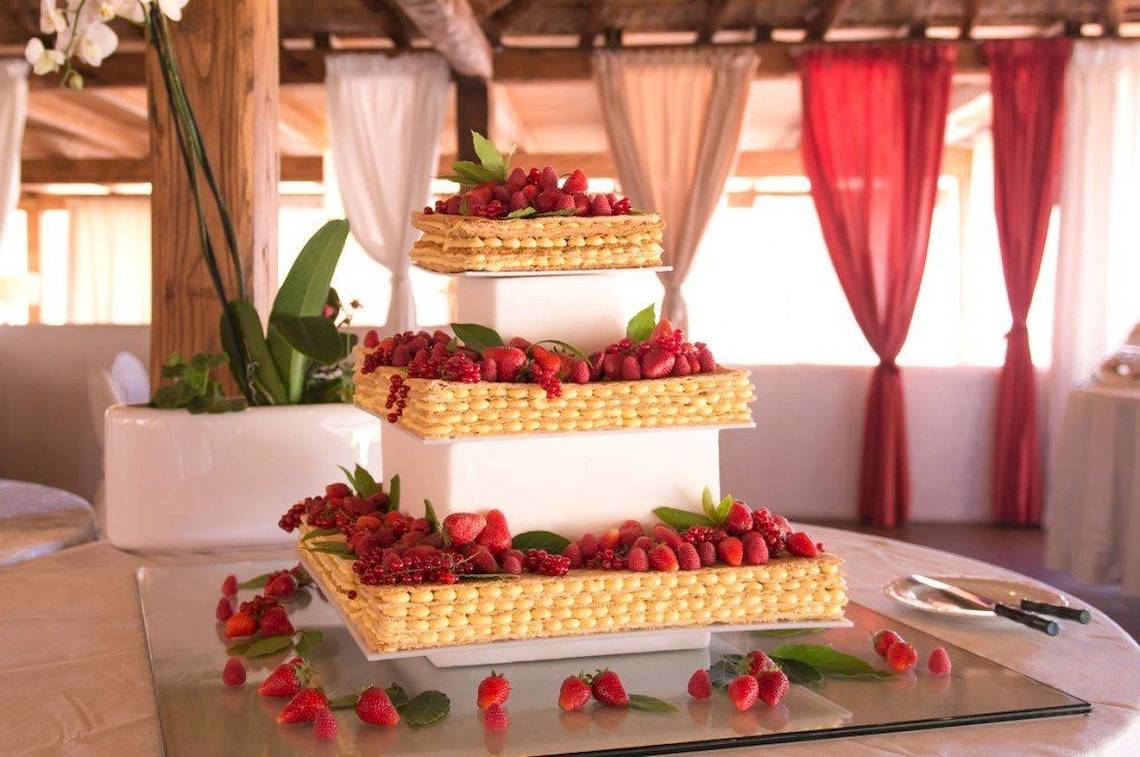 Eine dreistöckige Hochzeitstorte im Hotel Ollastu Resort mit Früchten und Blättern verziert.