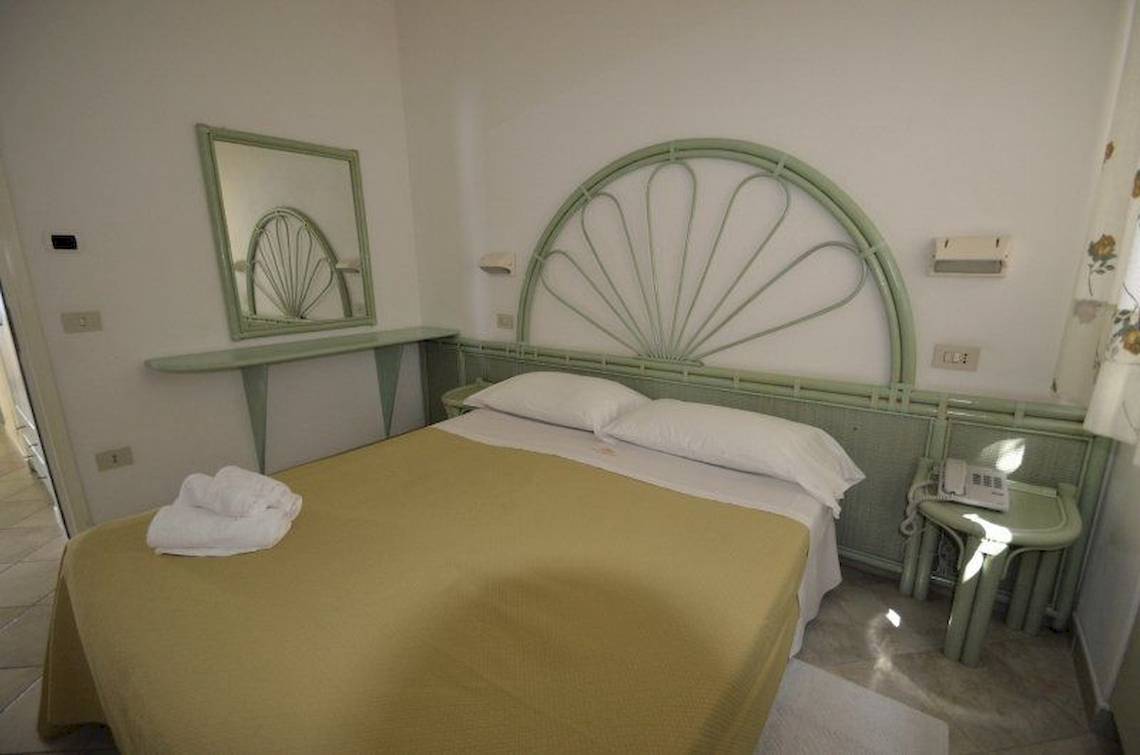 Ein Schlafzimmer im Hotel Cala di Volpe mit grünem Kopfteil, Bettwäsche und Spiegel