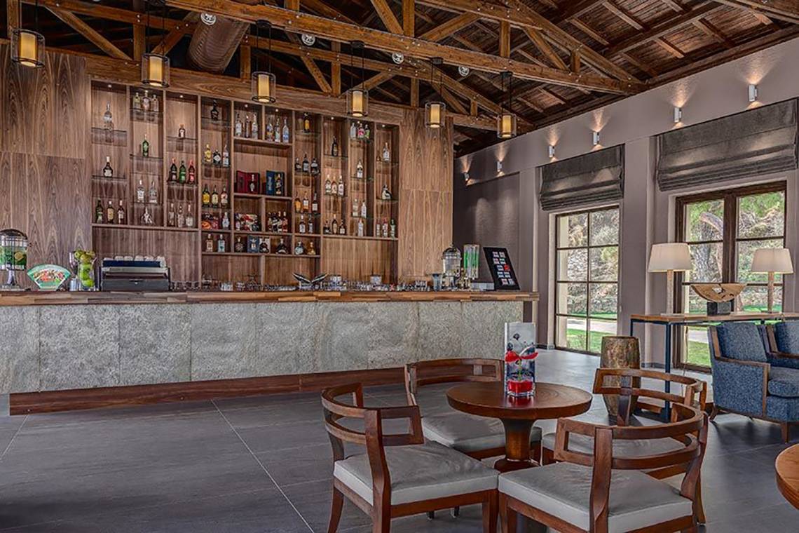 Innenansicht der Bar im Rixos Premium Tekirova Hotel mit Tresen, Holzmöbeln und großen Fenstern.