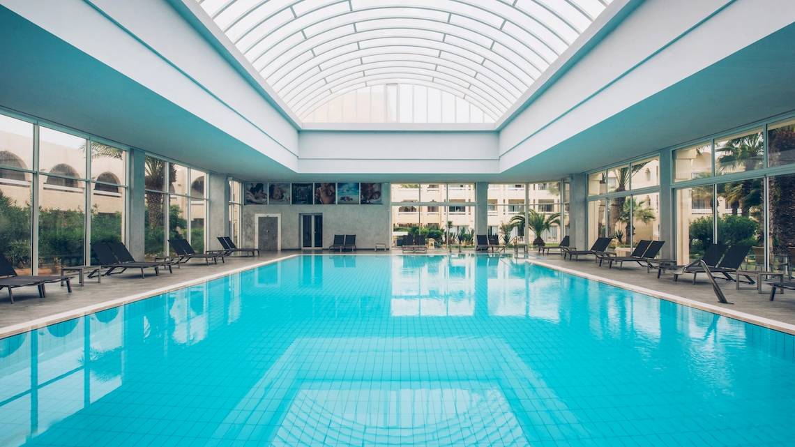 Ein großer Swimmingpool im Iberostar Mehari Djerba Hotel mit Liegestühlen und Glaswänden
