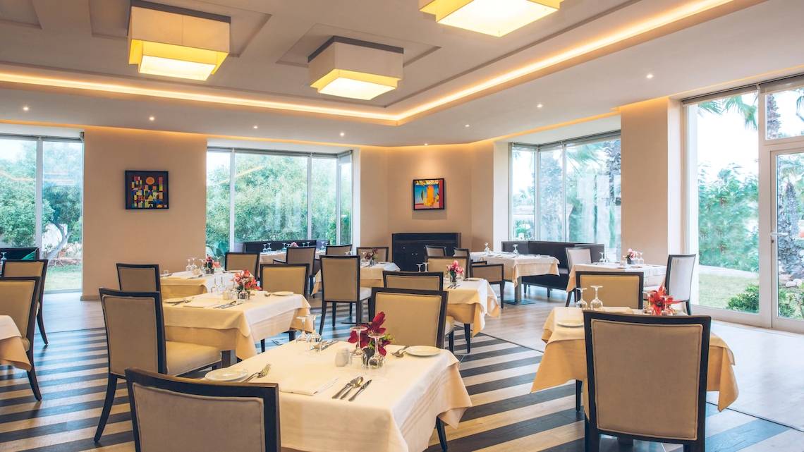 Innenansicht des Restaurants im Iberostar Mehari Djerba Hotel mit gedeckten Tischen und Glaswänden.