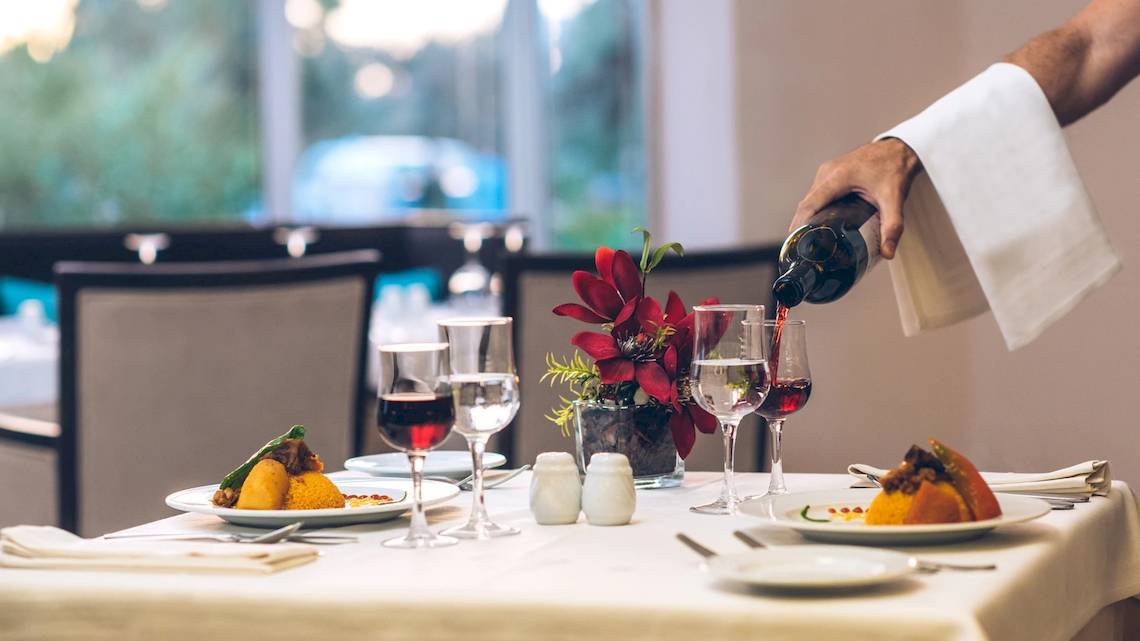Ein Restauranttisch im Iberostar Mehari Djerba mit einem Gast, der Wein einschenkt.
