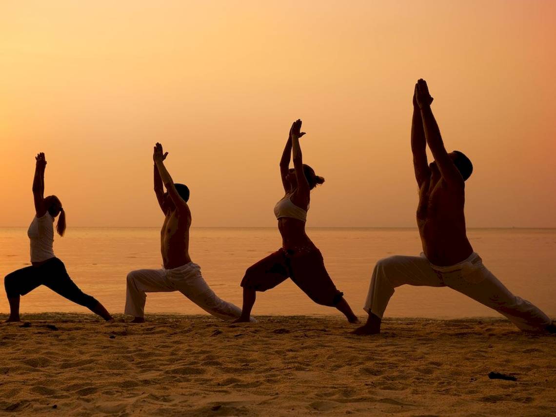 Vier Personen machen Yoga am Strand bei Sonnenuntergang.
