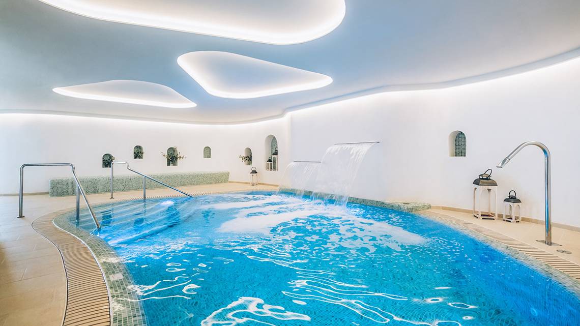 Ein Hallenbad im Iberostar Selection Fuerteventura Palace mit Wasserfall und modernen Beleuchtungselementen.