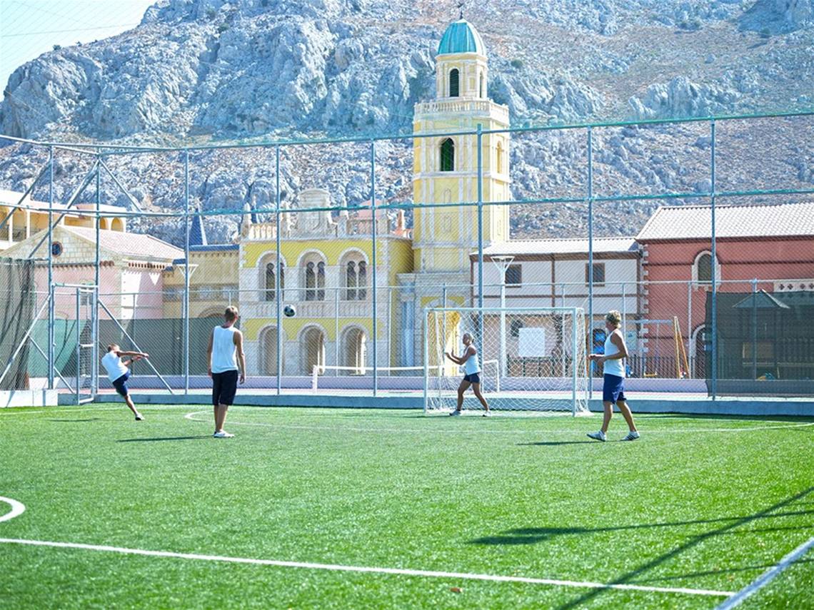 Fussballspieler spielen auf einem Fussballplatz im Freien vor einem historischen Gebäude.
