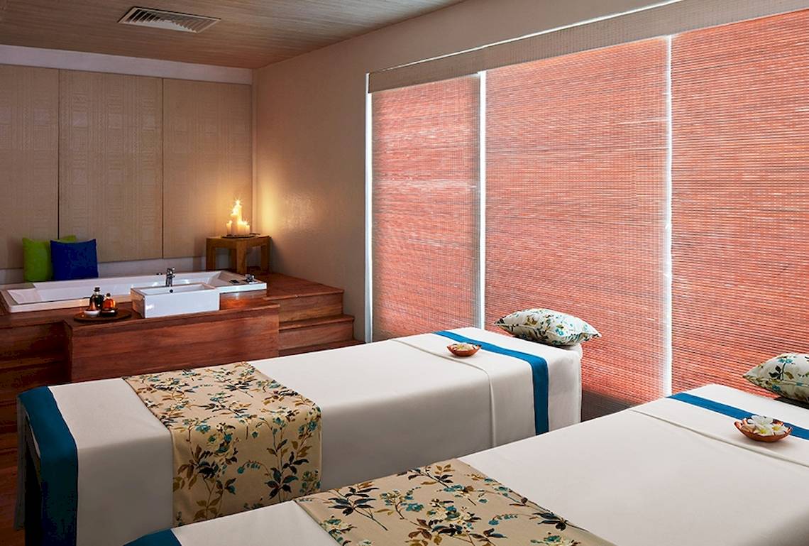 Spa-Behandlungsraum im Jetwing Blue mit zwei Betten, Badewanne und orangefarbenen Rolläden.