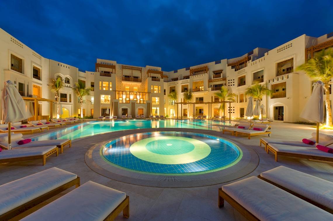 Außenpool des Sifawy Boutique Hotels bei Nacht mit beleuchteten Gebäuden und Lounge-Stühlen.