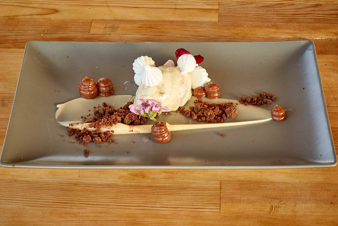 Ein Schokoladen-Dessert auf einem grauen Teller mit Eis, Schokoladenstücken und Blumendekor.