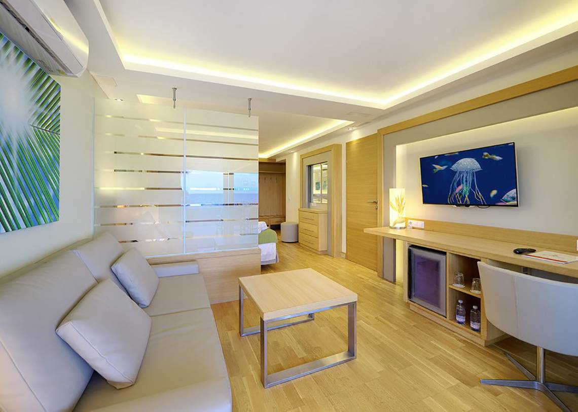 Inneneinrichtung eines Zimmers im Bull Costa Canaria & Spa Hotel mit Sofa, Couchtisch, Fernseher und Schreibtisch.