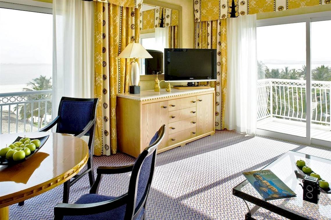 Innenansicht einer Suite im Hilton Salalah Resort mit Balkon, Fernseher und Tisch mit Früchten.