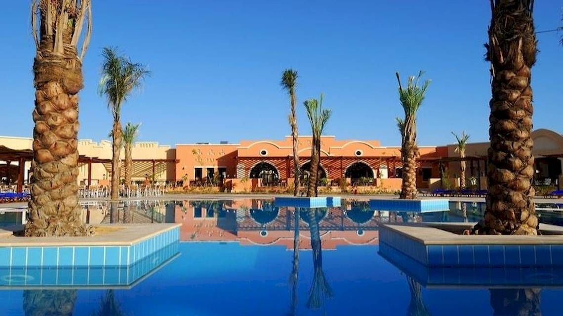 Außenpool des JAZ Neo Dar El Madina Hotels mit Palmen und orangefarbenem Gebäude.