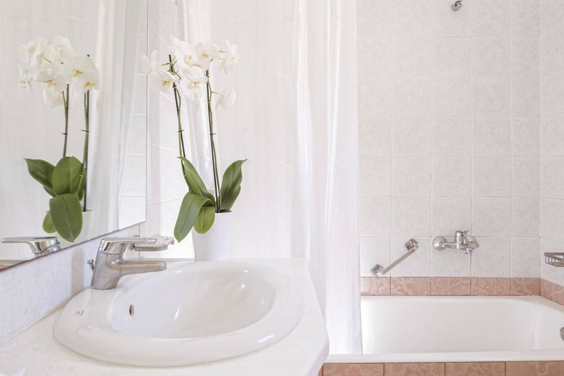 Badezimmer des Rhenia Mykonos Hotel mit weißer Wanne, Spiegel und Orchideen.